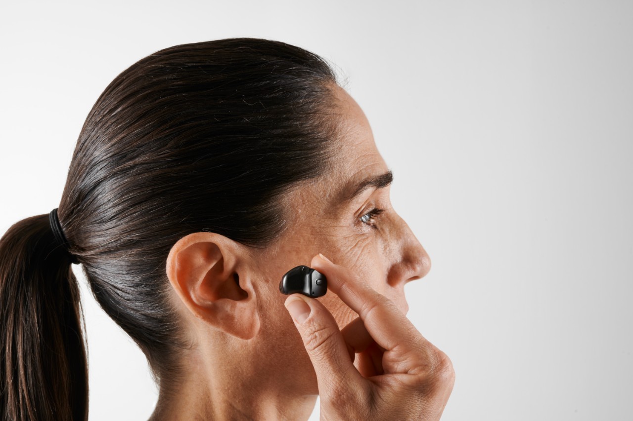 Homme senior tenant entre ses doigts un appareil auditif intra-auriculaire.