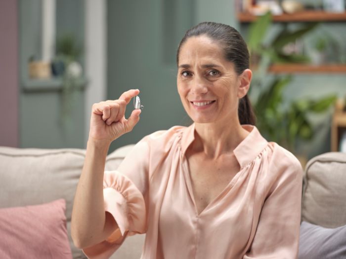 Femme souriante montrant une prothèse auditive