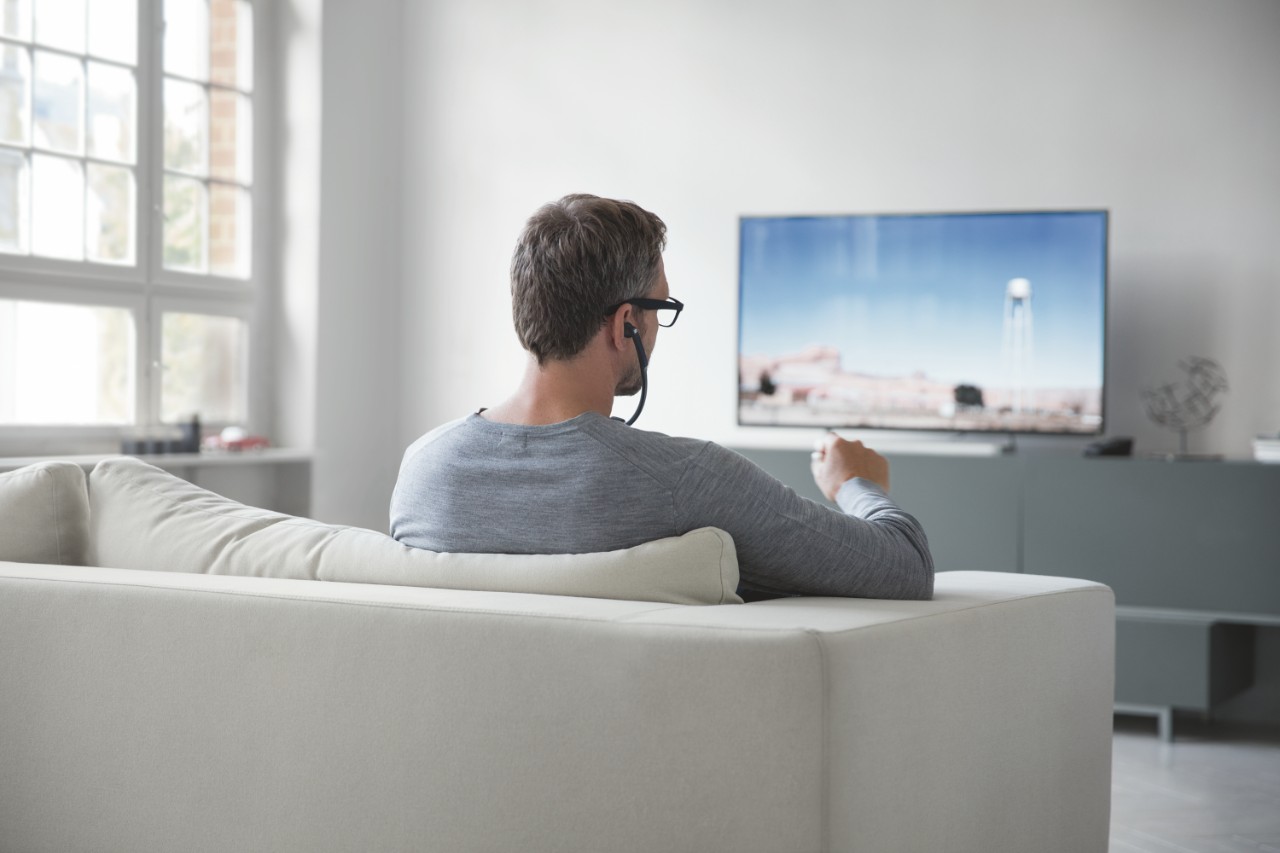 Un homme écoutant la télé dans son salon avec un casque audio à arceau