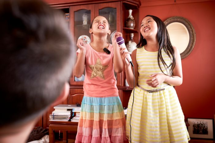 Deux jeunes filles, dont une portant un accessoire auditif, en train de faire du karaoké.