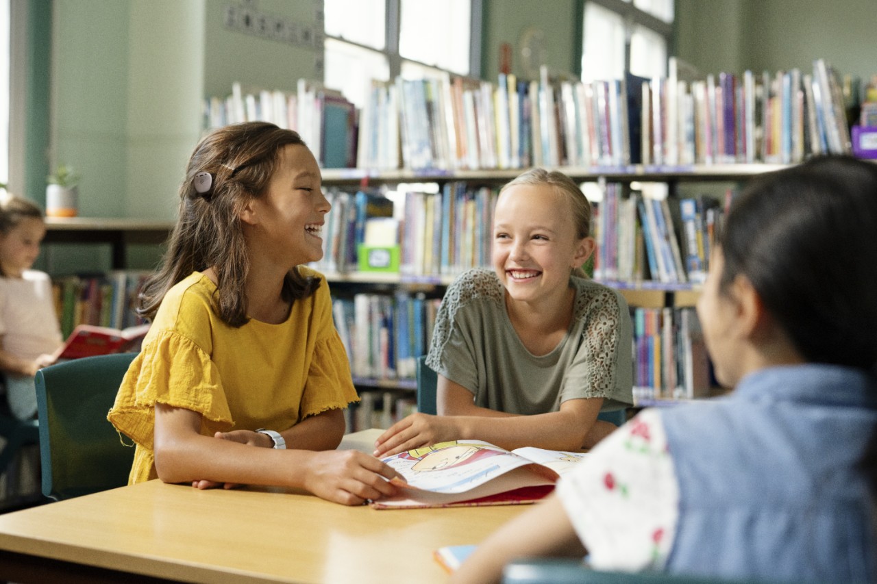 Trois petites filles à la table d'une bibliothèque