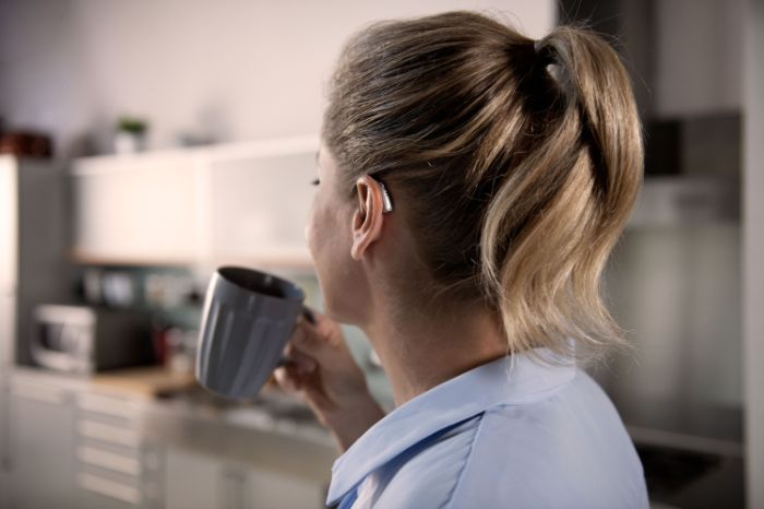Femme vue de profil portant une aide auditive à l'oreille gauche et tenant un mug à la main.