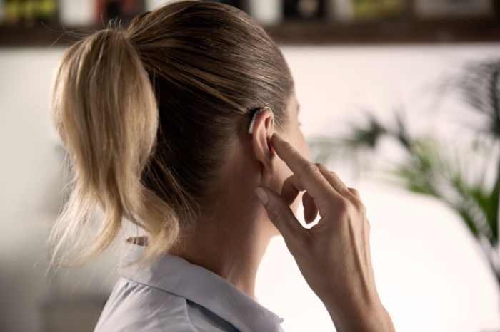 Femme vue de profil portant une aide auditive sur le contour de son oreille droite.