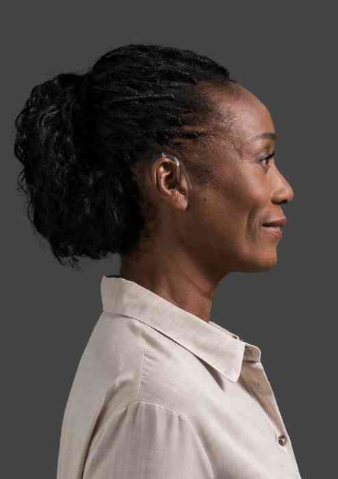 Profil d'une femme portant une chemise beige et un appareil BTE Amplifon.