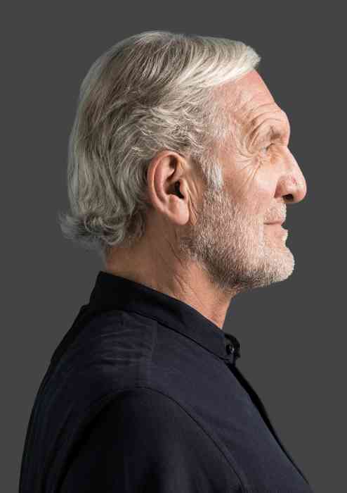 Profil d'un homme âgé dans un parc portant un appareil ITE Amplifon.