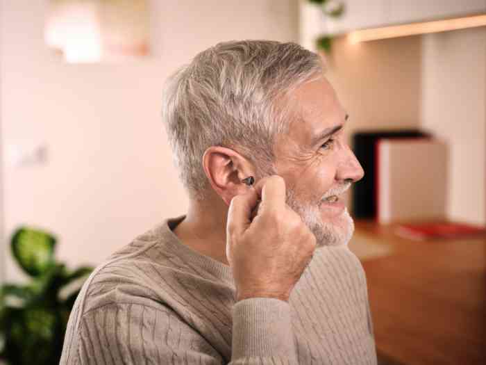 Ein Mann sieht sich im Spiegel an, während er ein Hörgerät in sein rechtes Ohr einsetzt.